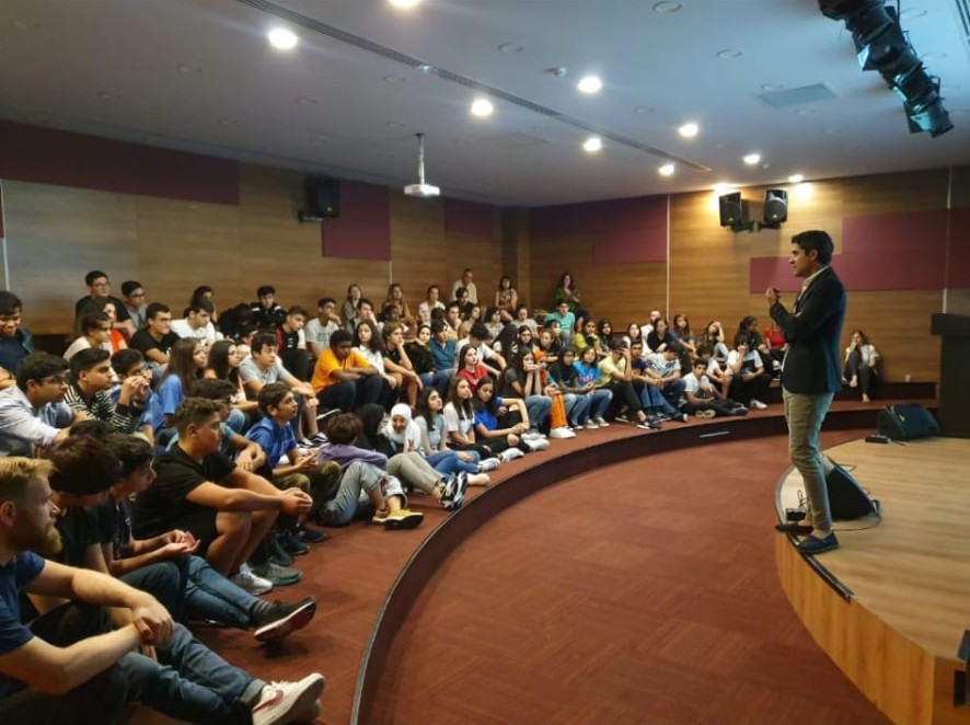 Hamada Zahawi speaking at the front of a full auditorium